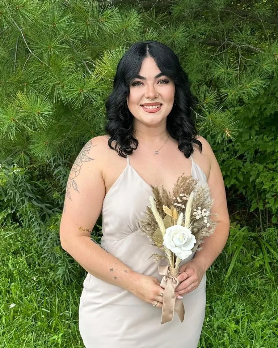 Paige Quillinan, smiling outdoors in front of pine trees